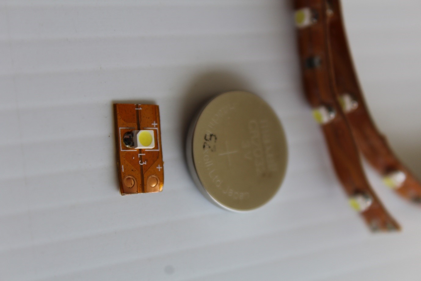 IMAGE: Close up of the LED (front), Battery 3-volt (round shaped-“coin”), copper tape with LED’s in the background.