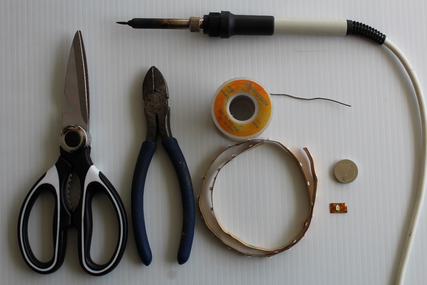 IMAGE: Basic tools required. LTR: Scissors, side cutter, solder, copper tape, battery (3 volts), LED (light). Switch & microcontroller (Picaxe) – not shown.